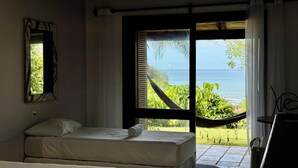 A bedroom with a bed, a window with a view of the sea, and a hammock outside. - Pousada Villa Agrifóglio (Imbituba)