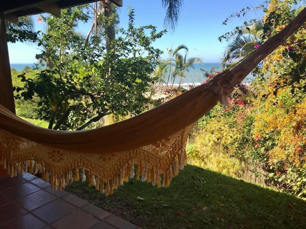 Un hamac est suspendu au-dessus d’une terrasse carrelée, offrant une vue sur un jardin luxuriant et l’océan.