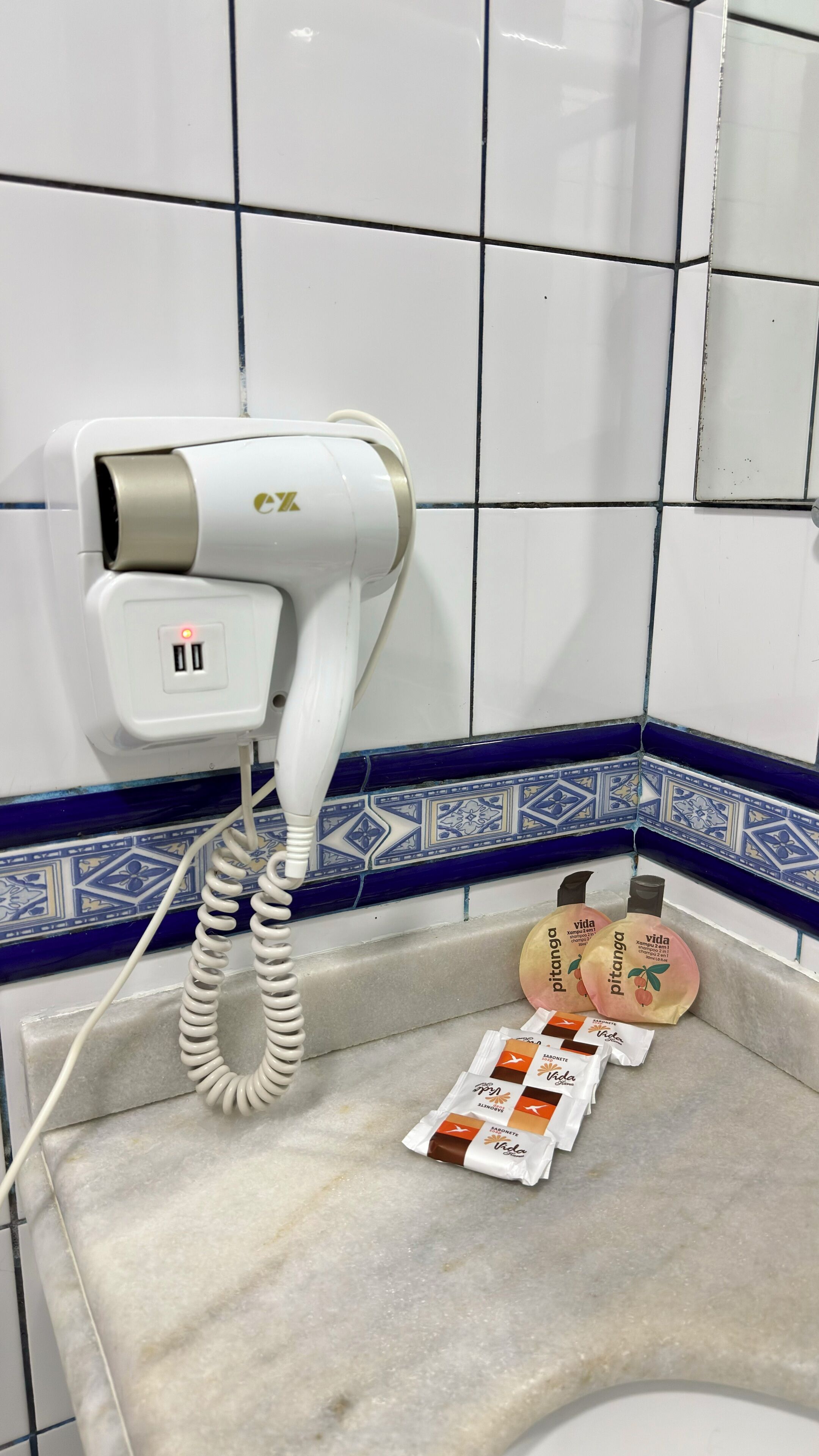 A hair dryer on a wall socket, a tiled wall with a blue and white pattern, and a countertop with packaged items.