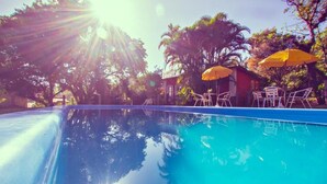 A clear blue pool with sun shining through the trees, surrounded by yellow umbrellas and white chairs. - Pousada Villa Agrifóglio (Imbituba)