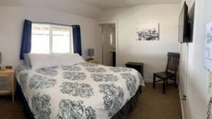 A bedroom with a bed, a chair, a nightstand, a window with curtains, and a wall-mounted picture. - The Idaho City Hotel (Idaho City)