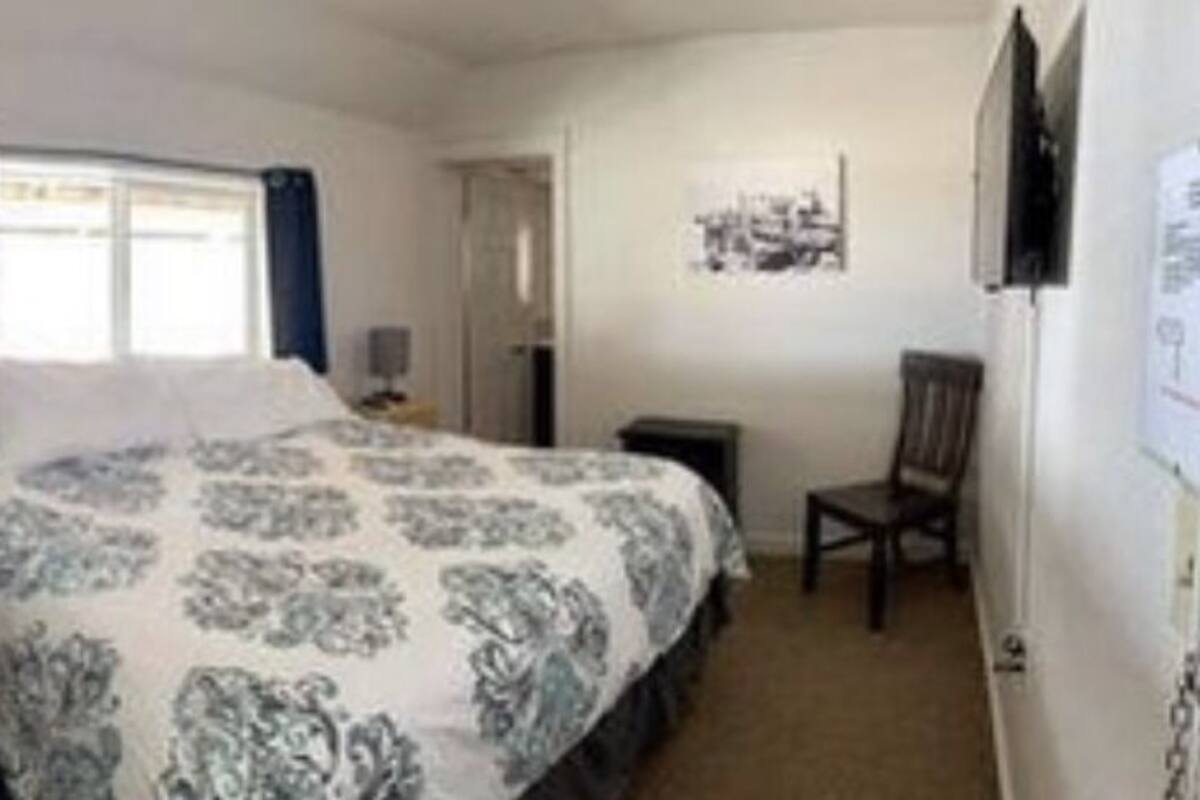 A bedroom with a bed, a chair, a nightstand, a window with curtains, and a wall-mounted picture.