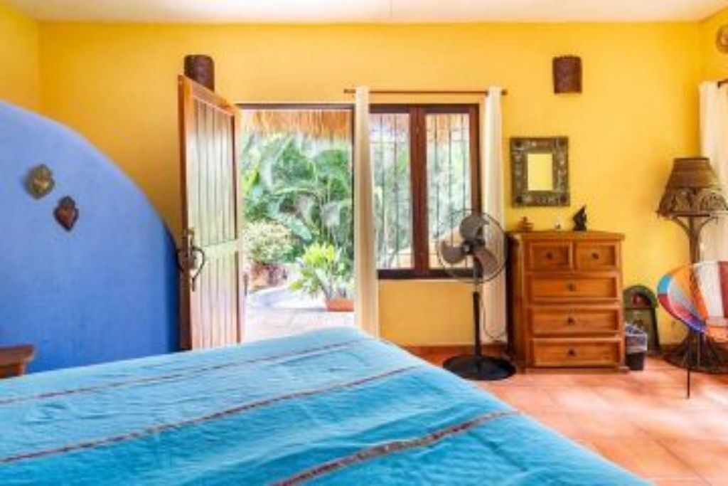 A bedroom with a bed, a dresser, a fan, and a view of the outdoors.