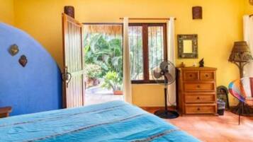 A bedroom with a bed, a dresser, a fan, and a view of the outdoors.