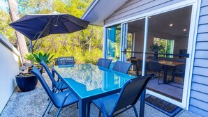 A glass-top dining table with chairs, a black umbrella, and potted plants in an outdoor patio area. - Kiali @ Cape Villas Dunsborough (Dunsborough)