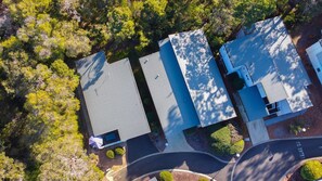 An aerial view of a residential area with three houses, a curved driveway, and surrounding greenery. - Kiali @ Cape Villas Dunsborough (Dunsborough)