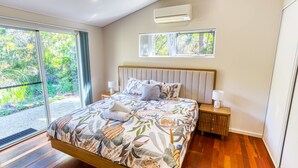 A modern bedroom with a large bed, two bedside tables, a window with a view of greenery, and an air conditioning unit on the wall. - Kiali @ Cape Villas Dunsborough (Dunsborough)