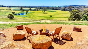 A patio with a fire pit, two wooden chairs, and large rocks. - Nannup Rise Holiday Home (Nannup)