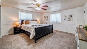 Un dormitorio con cama, mesitas de noche, ventilador de techo y obras de arte en las paredes.