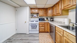 Cocina compacta con armarios de madera, estufa blanca, microondas y pileta de acero inoxidable.