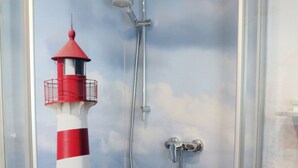 Una doccia con porta in vetro, un murale con un faro rosso e bianco a righe e un asciugamano sul pavimento.