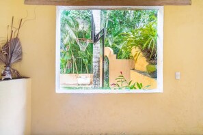 Enjoy a serene view of the lush garden from this room's window, featuring a beautiful outdoor landscape with palm trees and tropical plants.