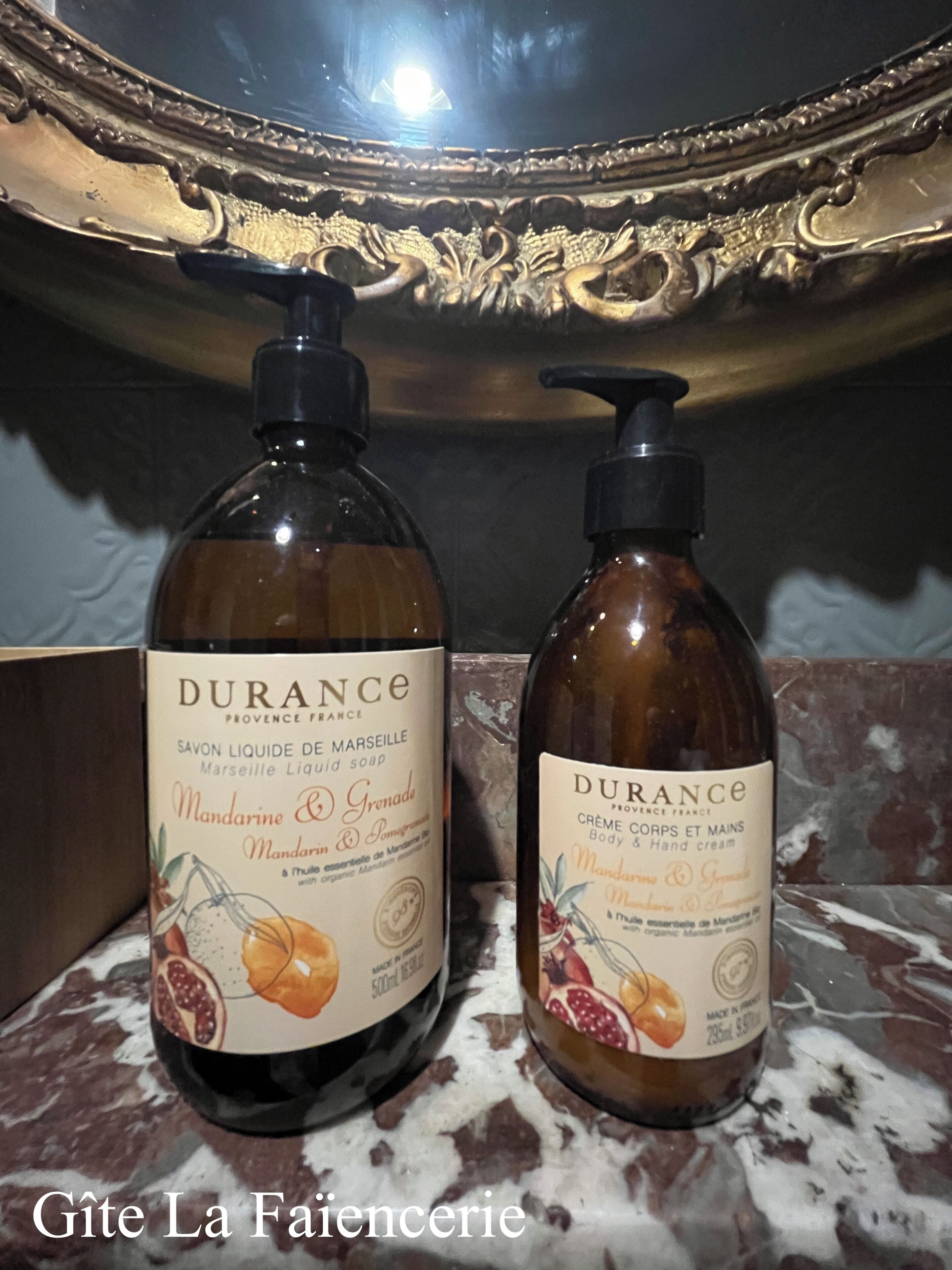 Two bottles of Durance body and hand cream on a marble surface with a decorative mirror in the background.