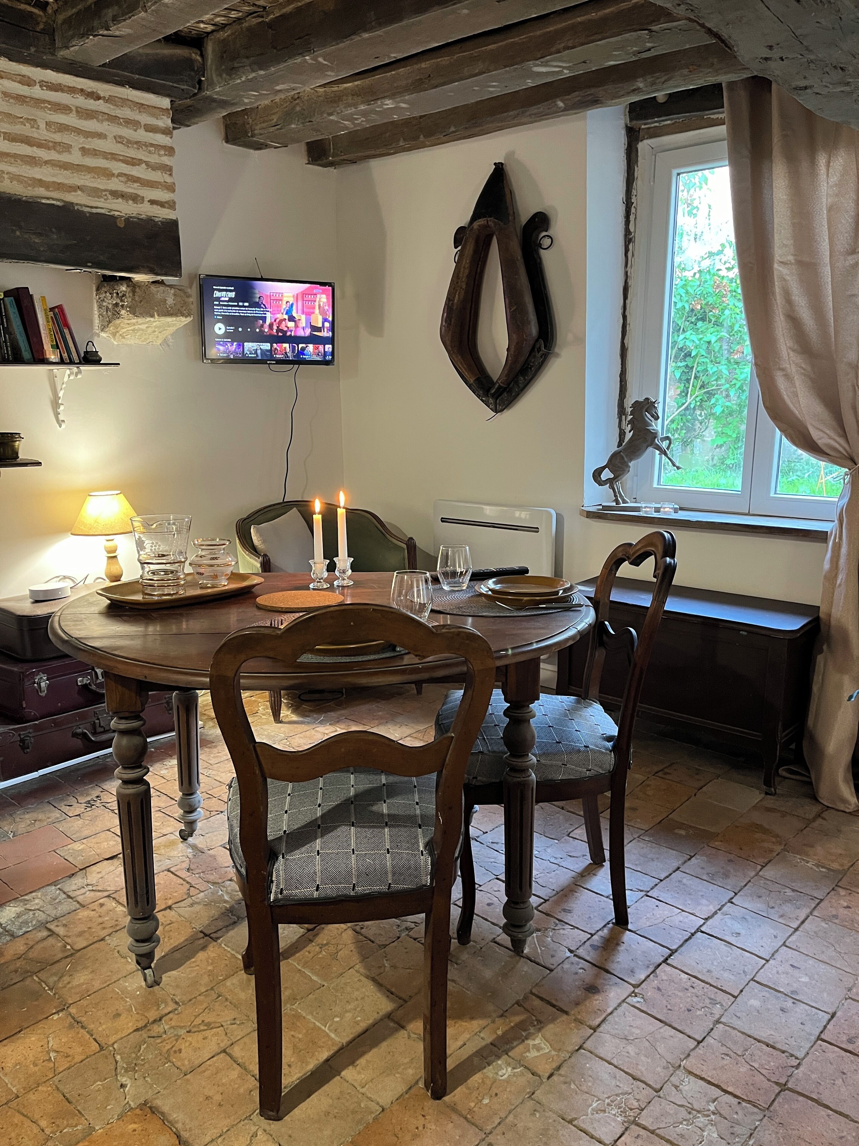 Un comedor con mesa de madera, sillas, televisor montado en la pared y una ventana con cortinas.