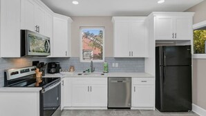 A modern kitchen with white cabinets, stainless steel appliances, and a window providing natural light. - Spacious Home on Gervais | 4BR 2BA | Downtown (Columbia)