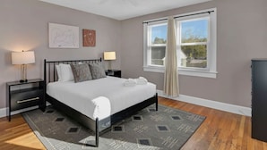 A bedroom with a bed, nightstands, a ceiling fan, a window with curtains, and a view of the outdoors. - Spacious Home on Gervais | 4BR 2BA | Downtown (Columbia)