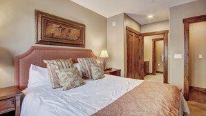 A hotel room with a large bed, a nightstand, a painting on the wall, and a wooden door leading to a bathroom. - Waterhouse 5109 (Breckenridge)