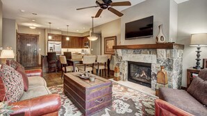 A living room with a fireplace, leather sofas, a coffee table, and a dining area with chairs and a kitchen in the background. - Waterhouse 5109 (Breckenridge)