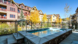 A swimming pool with a stone border, surrounded by a metal fence, and adjacent to multi-story buildings with balconies. - Waterhouse 5109 (Breckenridge)