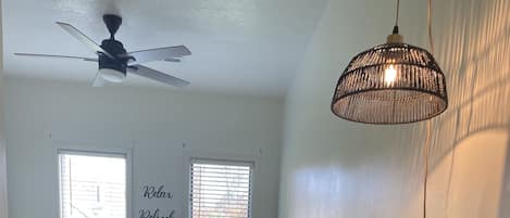 Una sala de estar moderna con un sofá, una mesa de centro, una mesa de comedor, un ventilador de techo y un amplio ventanal con persianas.