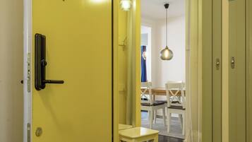 Una puerta amarilla que da a una habitación con una mesa de comedor y sillas, una lámpara colgante y una alfombra pequeña.