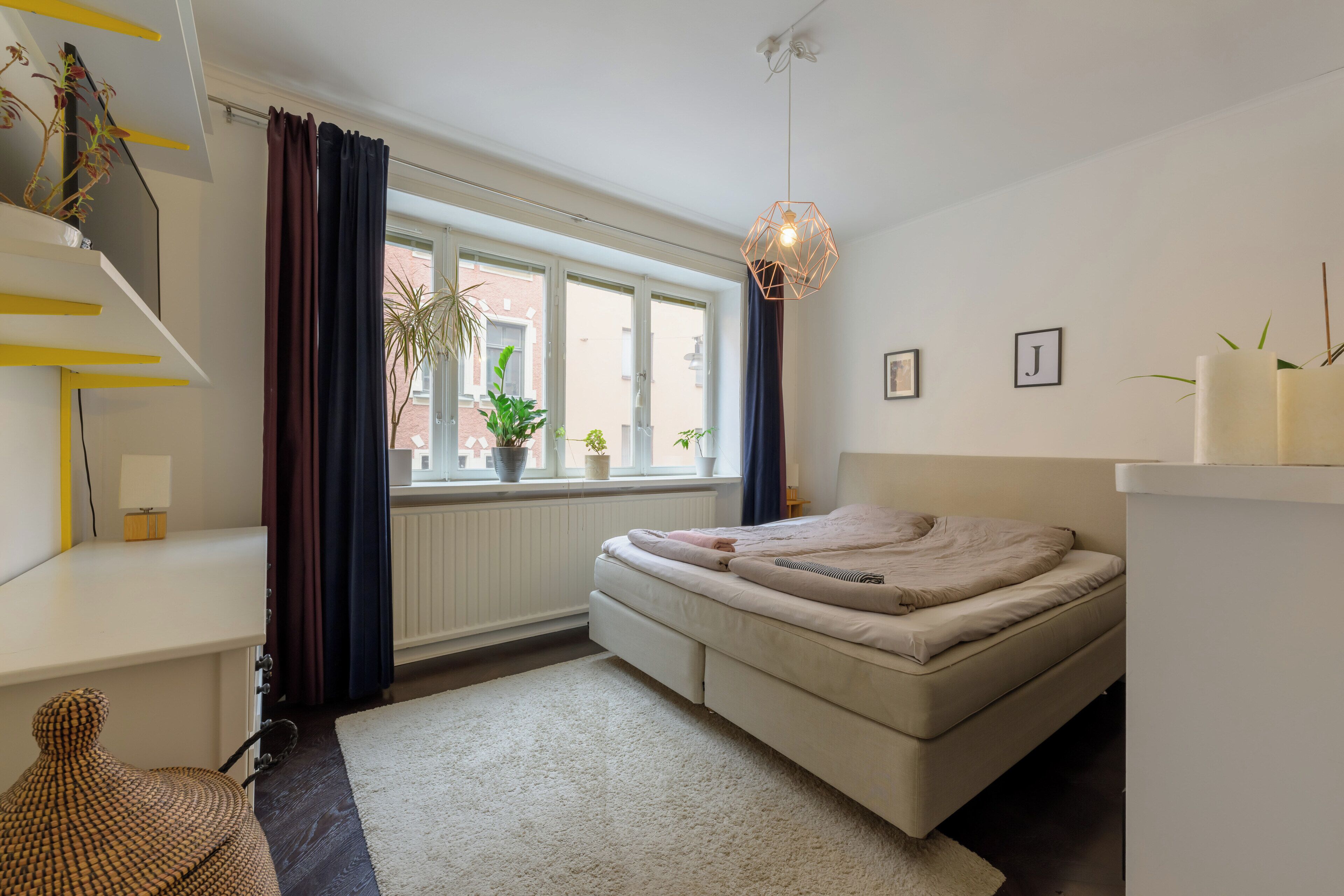 A modern bedroom with a bed, a window with curtains, a hanging light fixture, and a radiator.