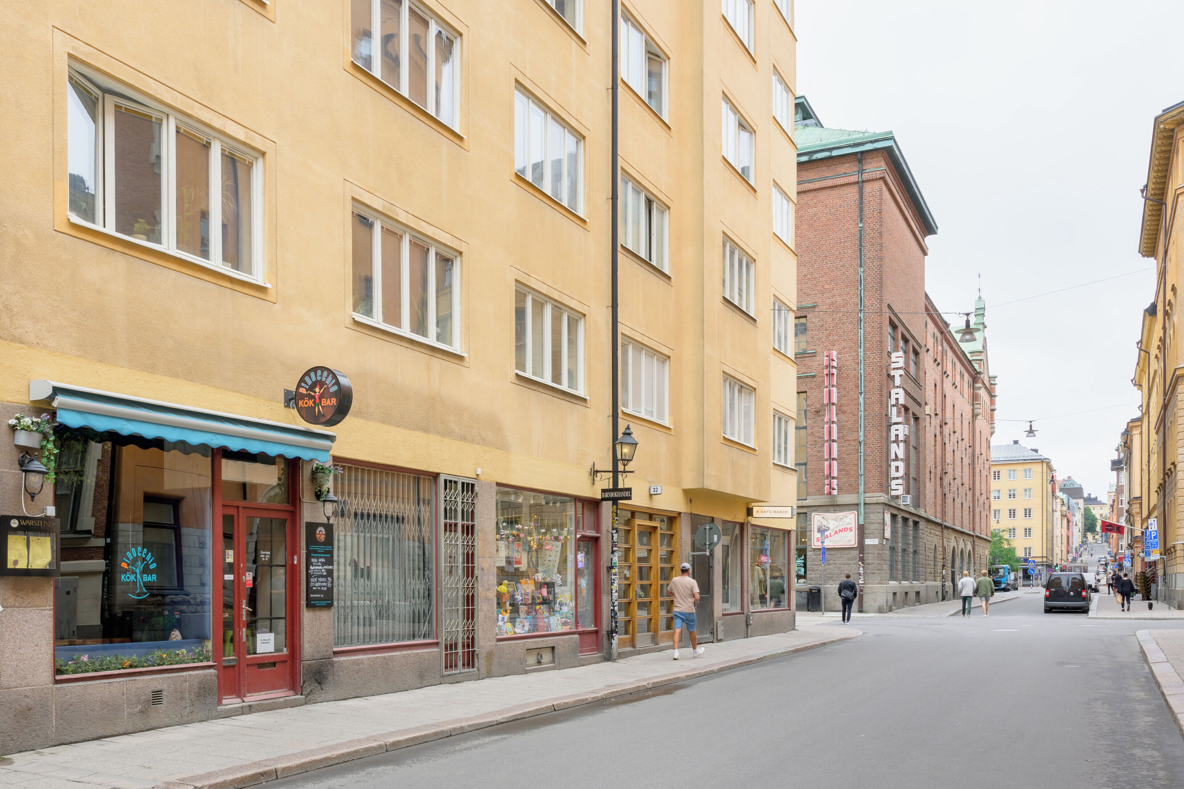 A street with yellow buildings, a shop with a red awning, and a sign that reads "KOK BAR".