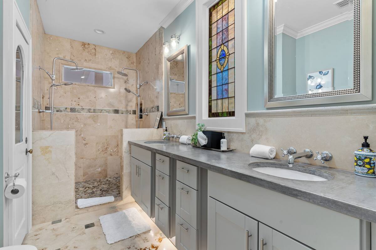 A bathroom with a shower, two sinks, a large mirror, and a stained glass window.