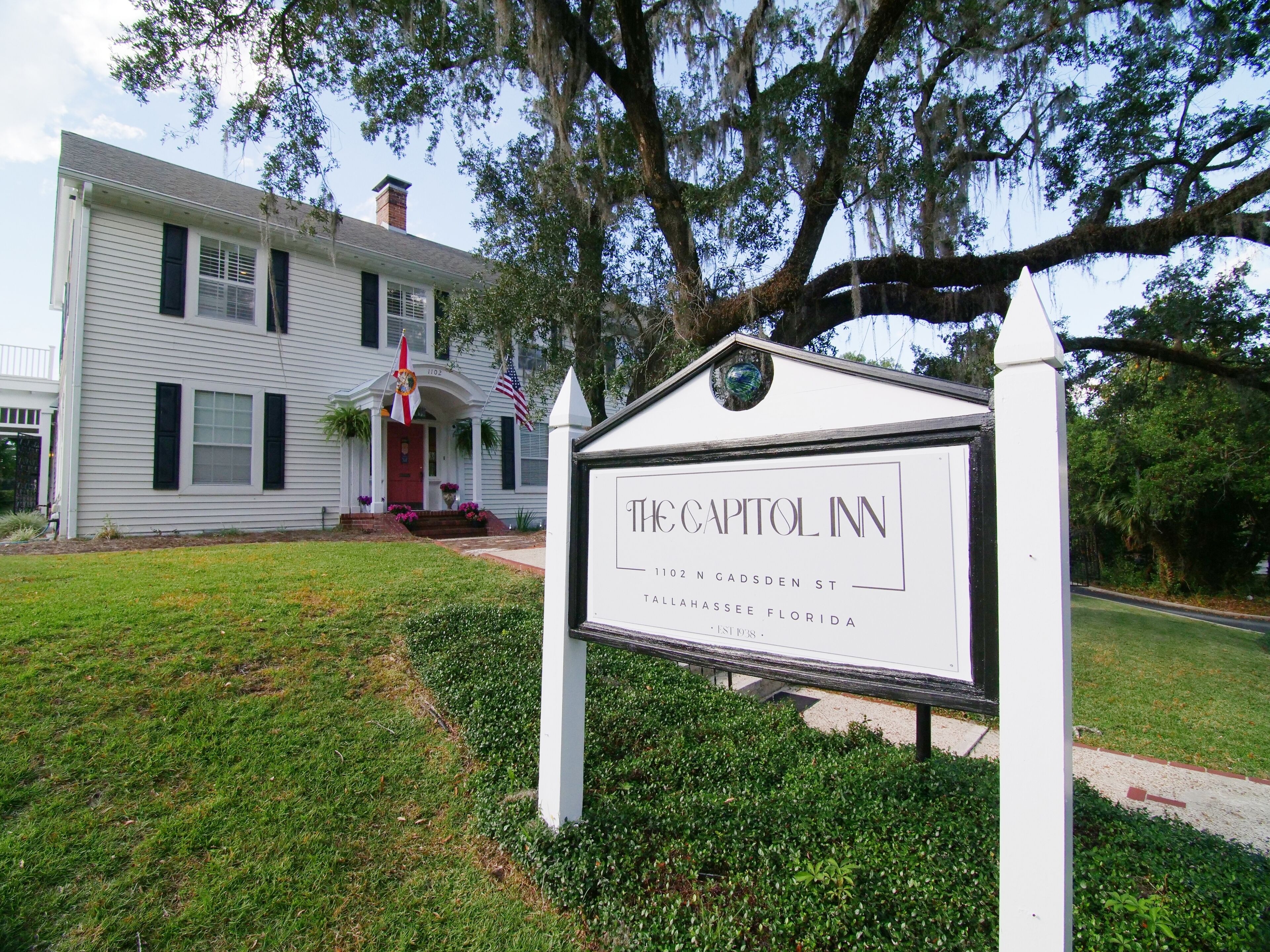 Letrero de The Capitol Inn, un edificio blanco con puerta roja, ubicado en 902 N Gadsden St, Tallahassee, Florida.
