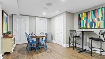A dining area with a wooden table and blue chairs, a bar with stools, and a colorful abstract painting on the wall.