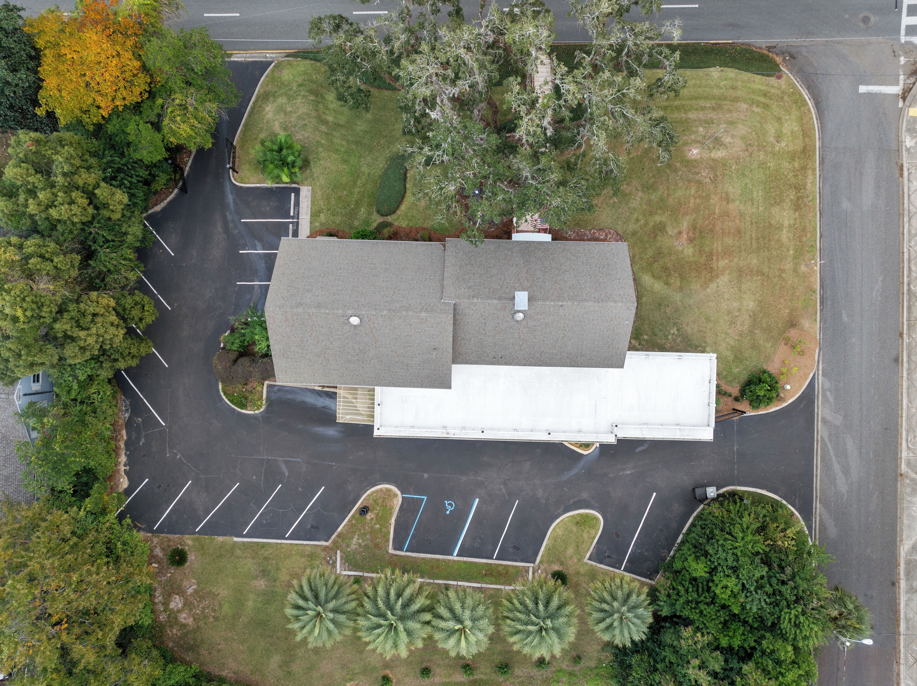 An aerial view of a building with a flat roof, surrounded by a parking lot and greenery.