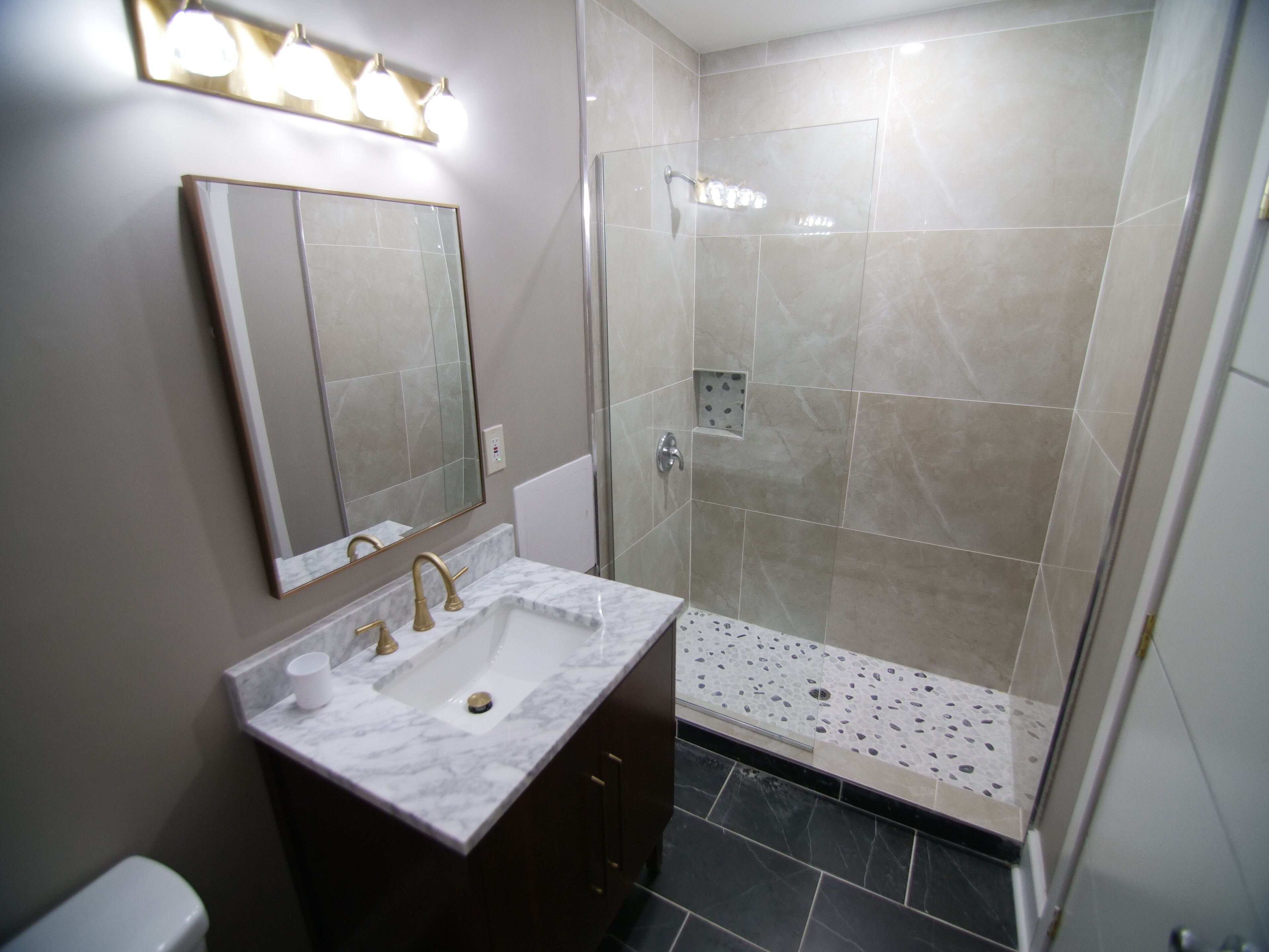 A modern bathroom with a marble sink, a large mirror, and a glass-enclosed shower area.