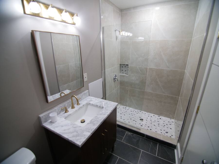 A modern bathroom with a marble sink, a large mirror, and a glass-enclosed shower area.