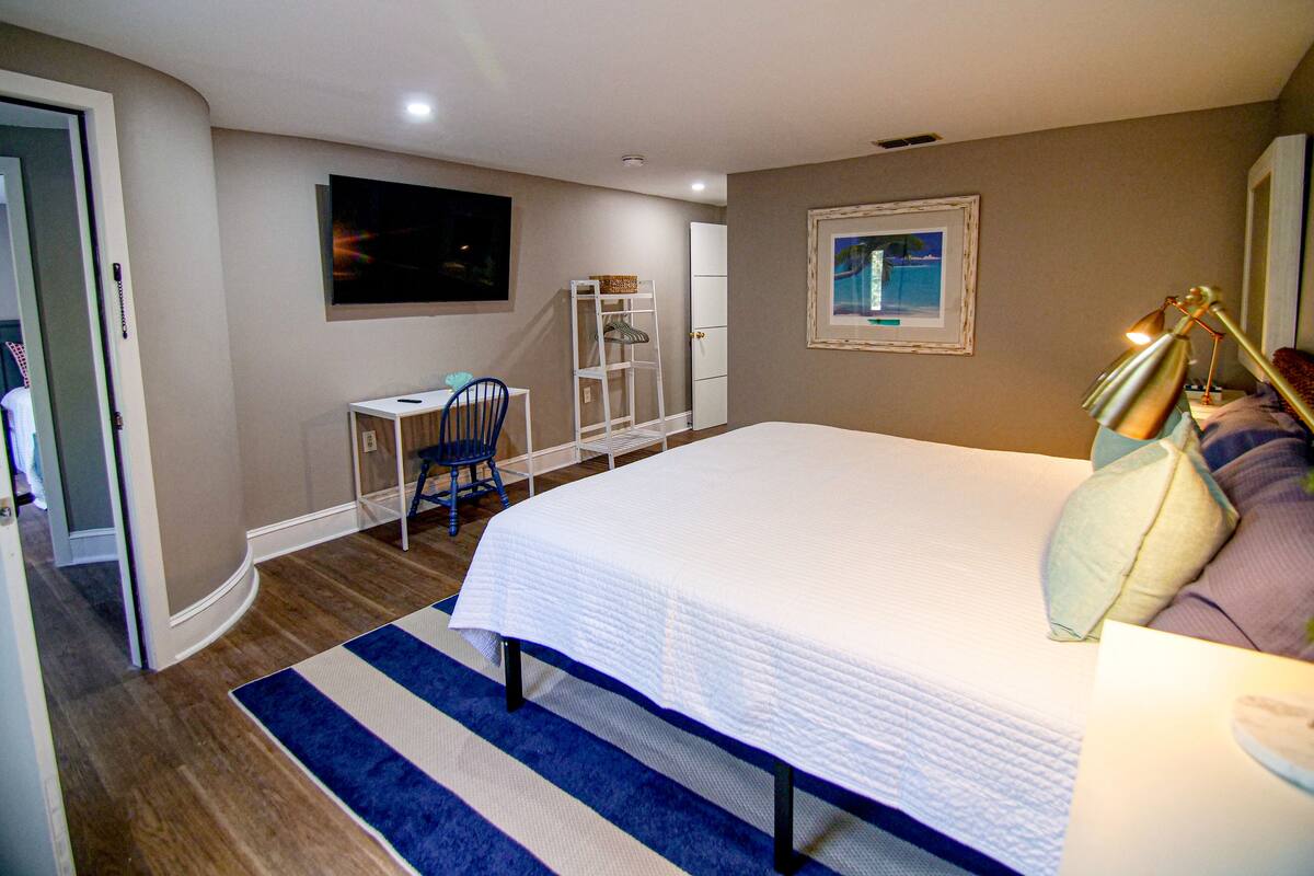A bedroom with a bed, a desk, a chair, a shelf, and a painting on the wall.