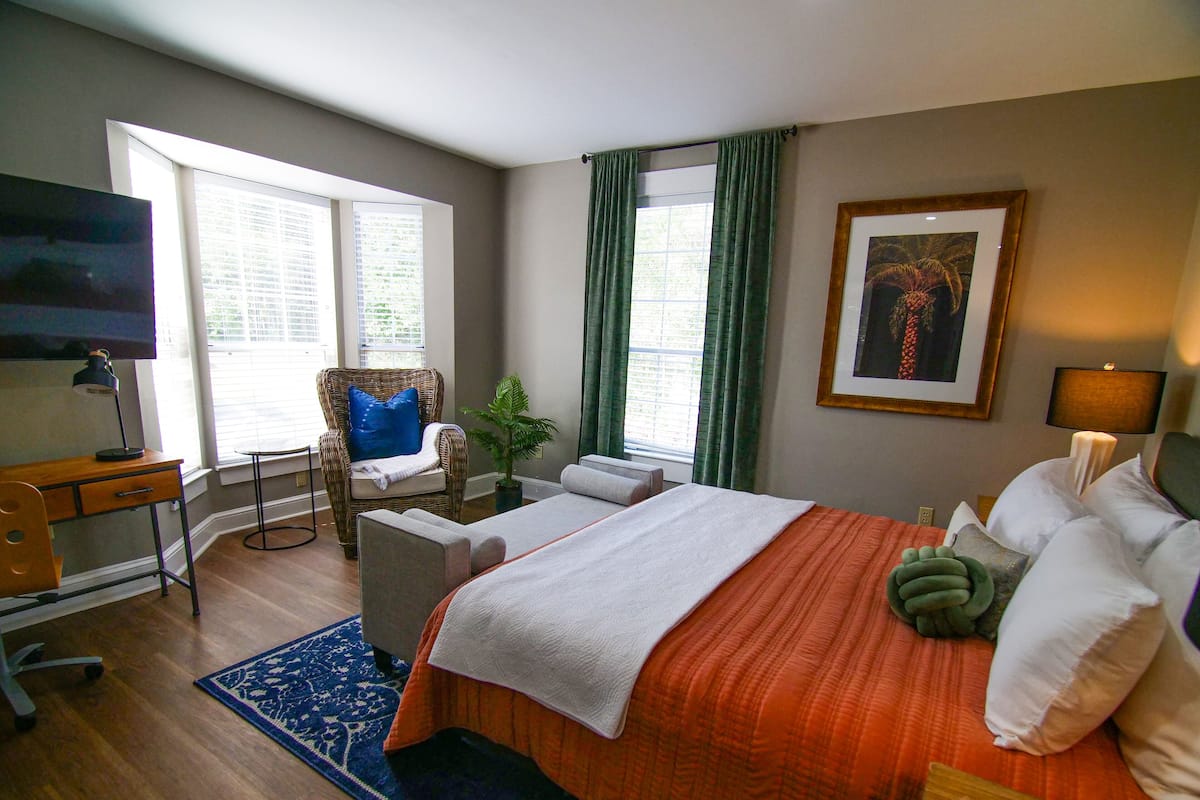 A hotel room with a bed, a desk, a chair, a TV, and a window with curtains.