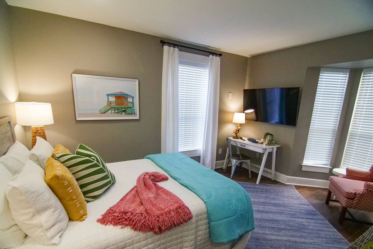 A hotel room with a bed, a desk, a chair, a TV, and a window with blinds.