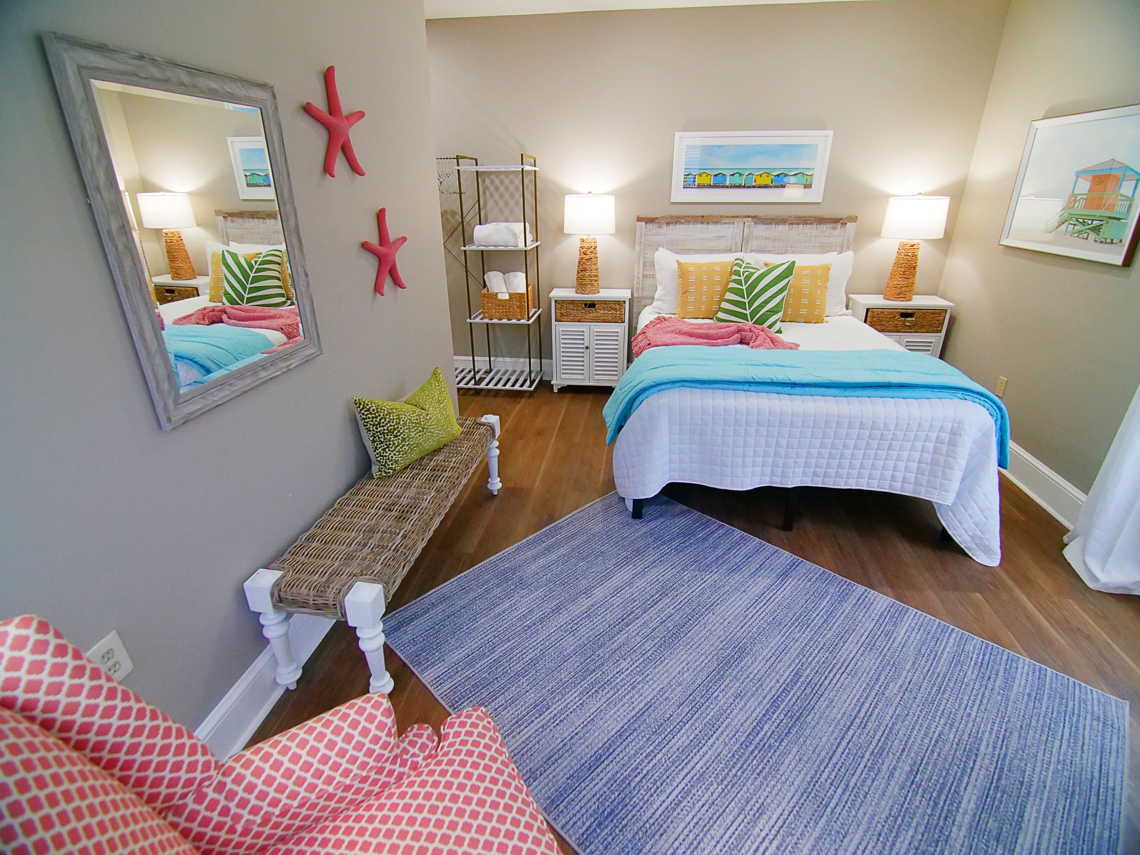 Une chambre avec deux lits, un banc, un miroir, des décorations en forme d’étoiles de mer et un tableau sur le thème de la plage.