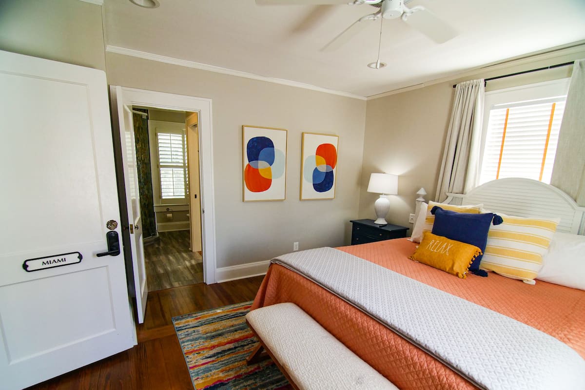 A bedroom with a bed, a bench, a nightstand, a lamp, and artwork on the wall.