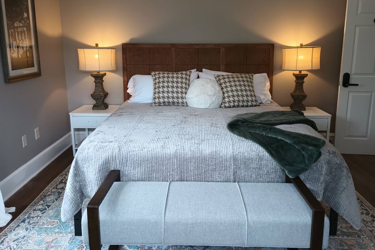 A neatly arranged bedroom with a large bed, two bedside lamps, a wooden headboard, and a bench at the foot of the bed.