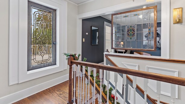 Una escalera con barandilla de madera y balaustres blancos, que conduce a una plataforma con una puerta de cristal decorativa y un espejo en la pared.