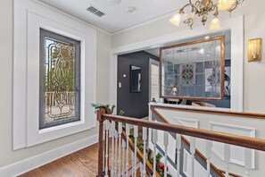 A staircase with a wooden handrail and white balusters, leading to a landing with a decorative glass door and a mirror on the wall. - The Capitol Inn Tallahassee (Tallahassee)
