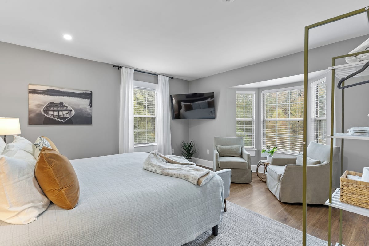 A bedroom with a bed, a TV, a chair, and a window.