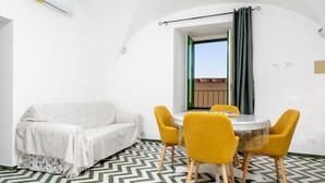 A compact living space with a sofa, a dining table with yellow chairs, and a patterned floor.