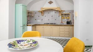 A kitchen with a teal refrigerator, yellow chairs, and a table with a fruit plate.