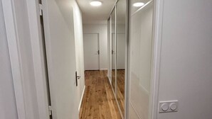 Un couloir étroit avec un plancher en bois, des murs blancs et une porte-fenêtre coulissante sur le côté droit.