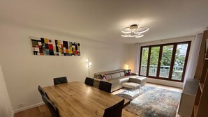 Un coin repas avec une table et des chaises en bois, un canapé et une grande fenêtre donnant sur un paysage verdoyant.