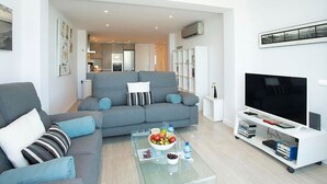 A modern living room with a grey sofa, a glass coffee table with a fruit bowl, and a white entertainment unit with a flat-screen TV.