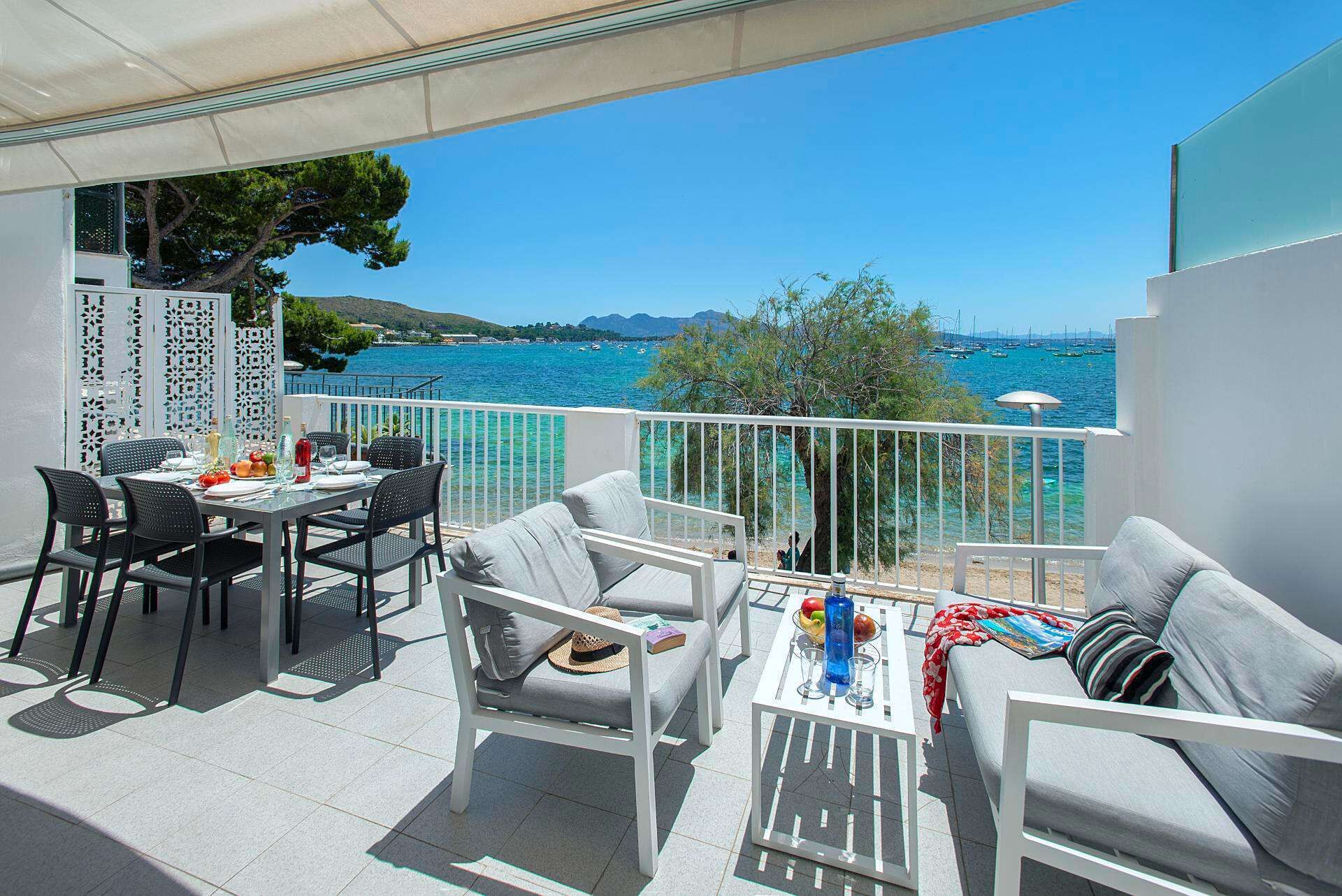 A balcony with a table set for two, a sofa, and a view of the sea and boats.