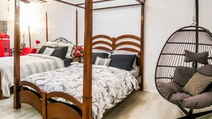 A four-poster bed with a white and black patterned bedspread, a hanging chair with cushions, and a red telephone booth in the background.