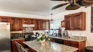 A kitchen with wooden cabinets, granite countertops, a stainless steel refrigerator, a microwave, a stove, and a ceiling fan.